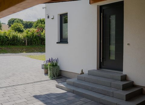Überdachter Eingangsbereich des Einfamilienhauses in Lichtenau mit anthrazitfarbener Haustür, Pflanzdeko und grauem Plattenbelag