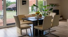 Essbereich mit viel Licht – Haus Lichten Offener Essbereich im Einfamilienhaus Lichtenau mit hellem Boden, moderner Sitzgruppe, Pflanzen und Blick nach draußen